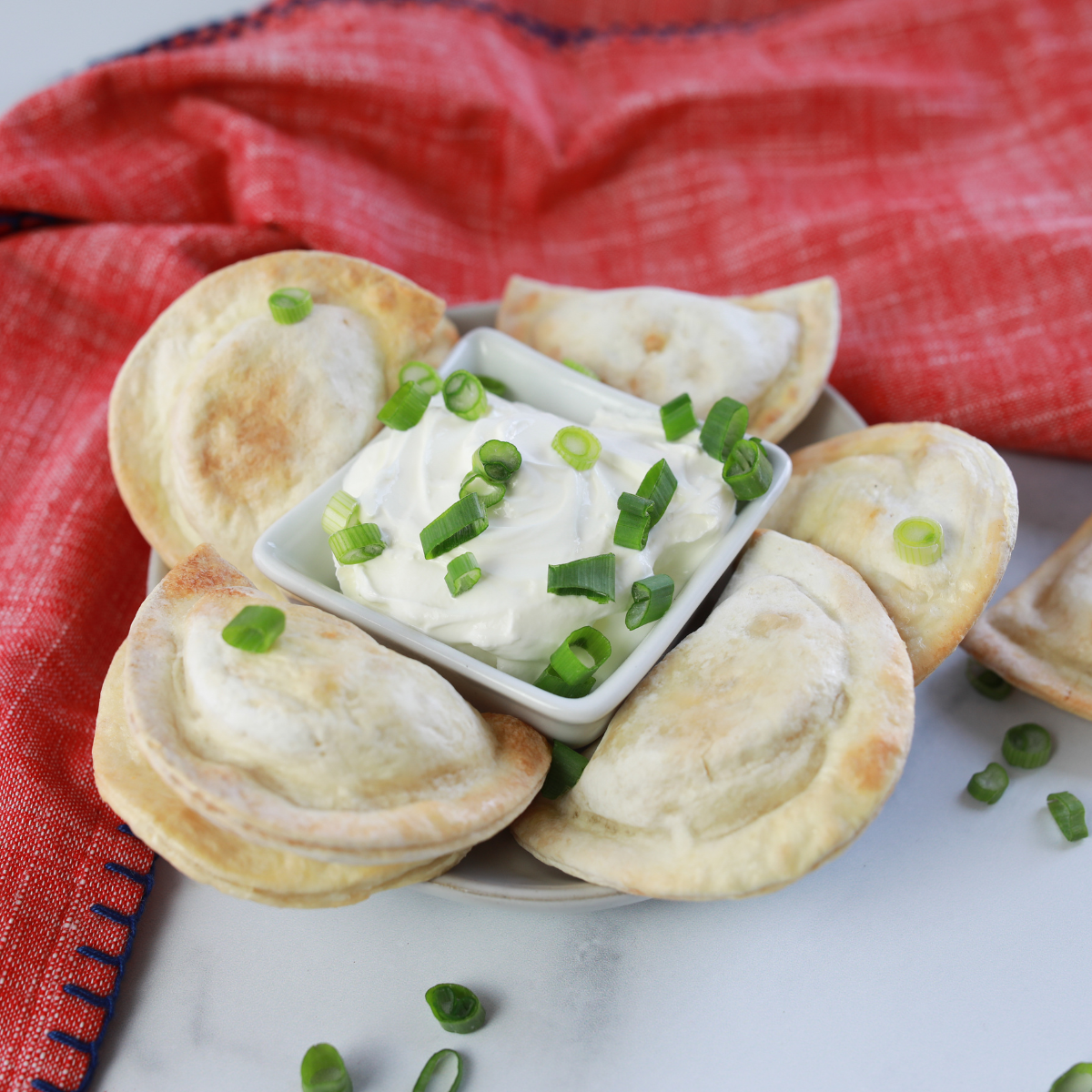 closeup: frozen pierogies cooked in air fryer with sour cream for dipping and green onion on top