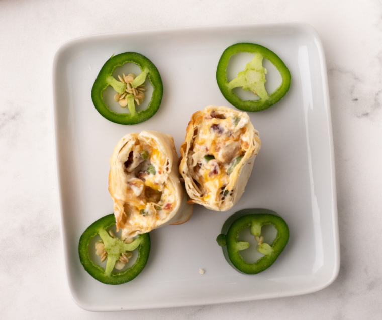  A plate of freshly air-fried jalapeno popper egg rolls garnished with fresh herbs, served with dipping sauce on the side.