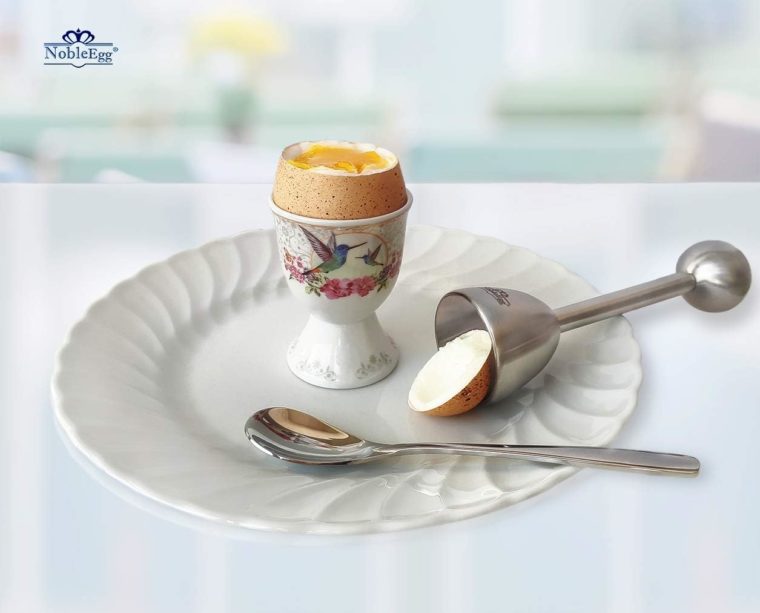 a soft boiled egg in an egg cup with its top removed with an egg top removing tool to the side