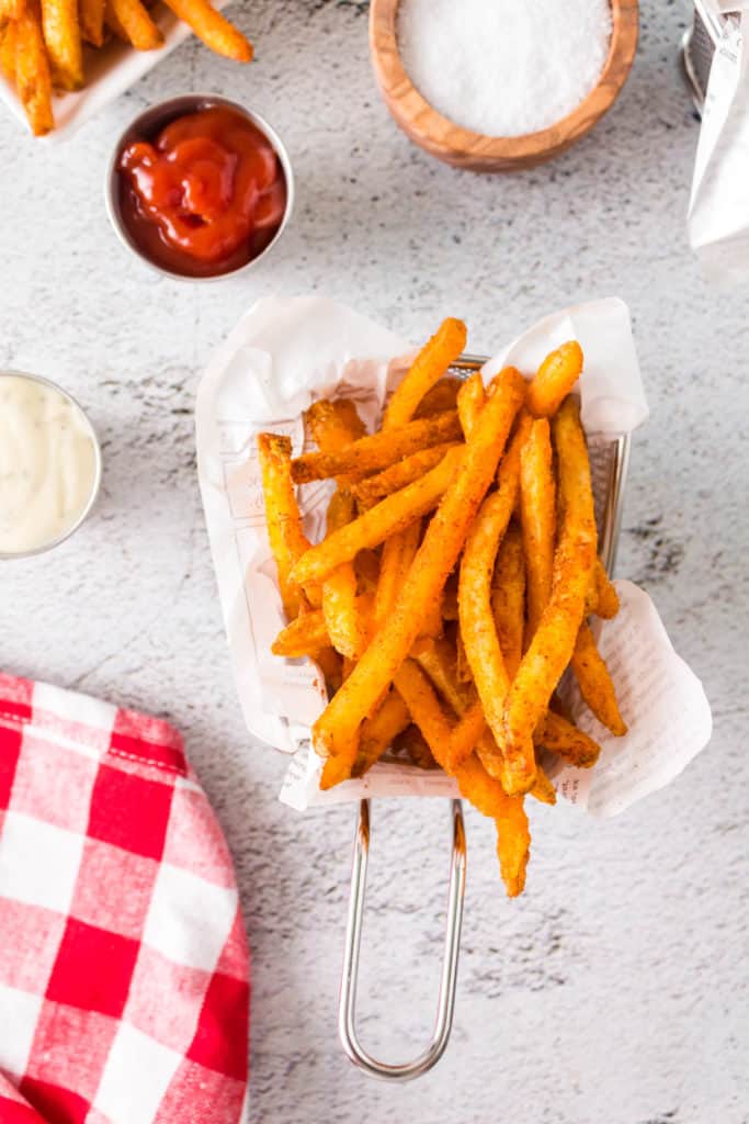 overhead: a small fry basket full of air fryer checkers fries with a red and white tea towel to the side