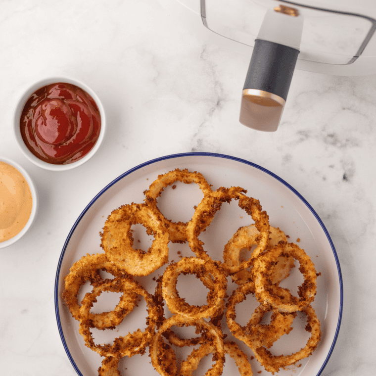 overhead: a plate full of air fried frozen onion rings with dipping sauces to the side