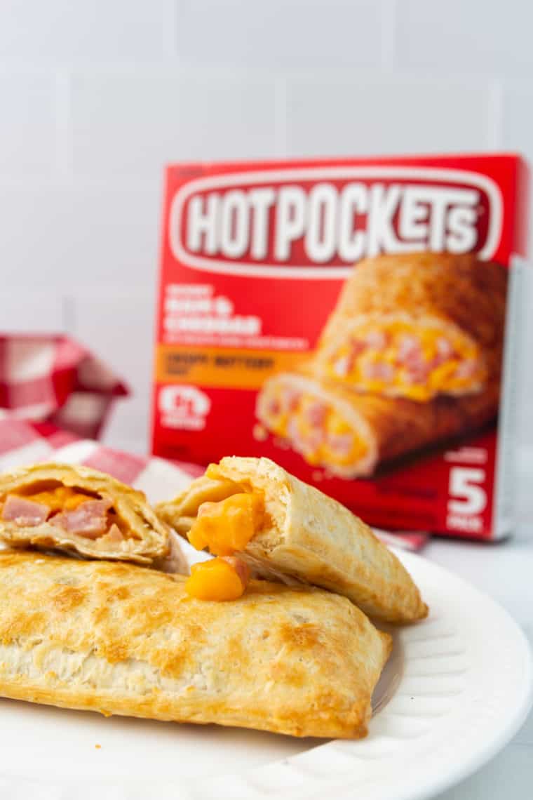 closeup: hot pockets made in air fryer on a white plate with one cut open so the ham and cheese filling is visible