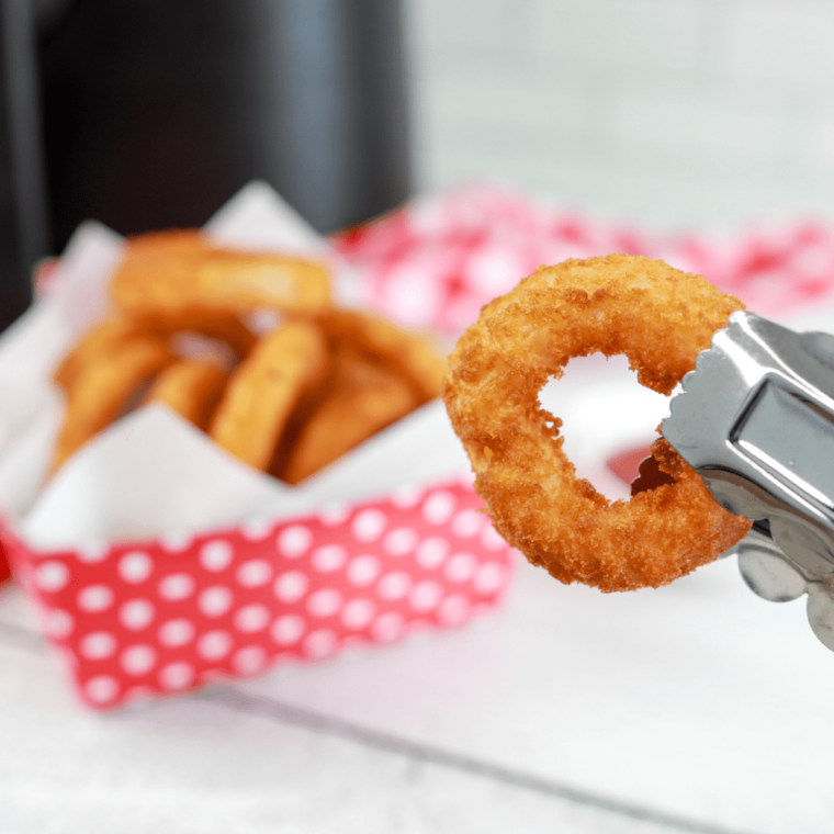 metal tongs holding an air fryer frozen onion ring with more in the background