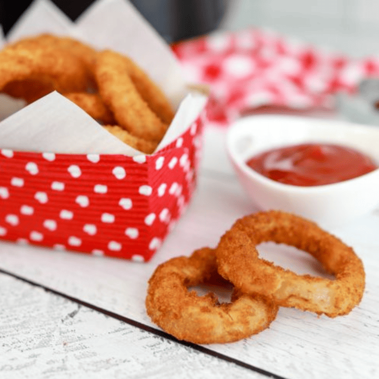 frozen onion rings in air fryer in a red and white box with ketchup to the side and two rings on the counter
