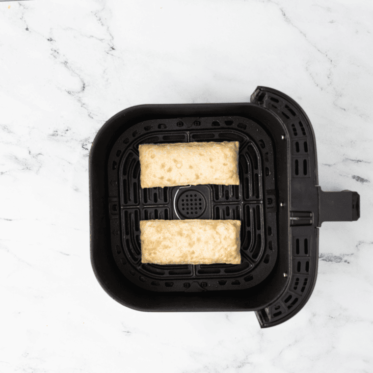 overhead: two frozen hot pockets in an air fryer basket before cooking on a white marble counter