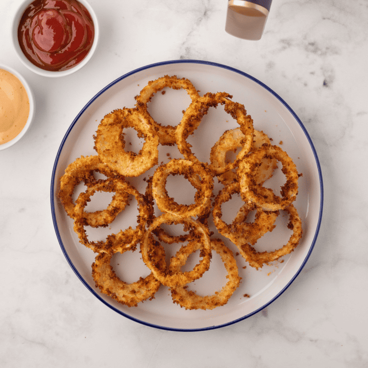 overhead: a plate of frozen onion rings made in air fryer with dipping sauces to the side