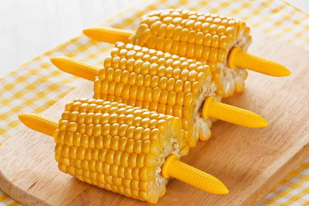 closeup: 3 small pieces of corn on the cob with corn holders on a cutting board