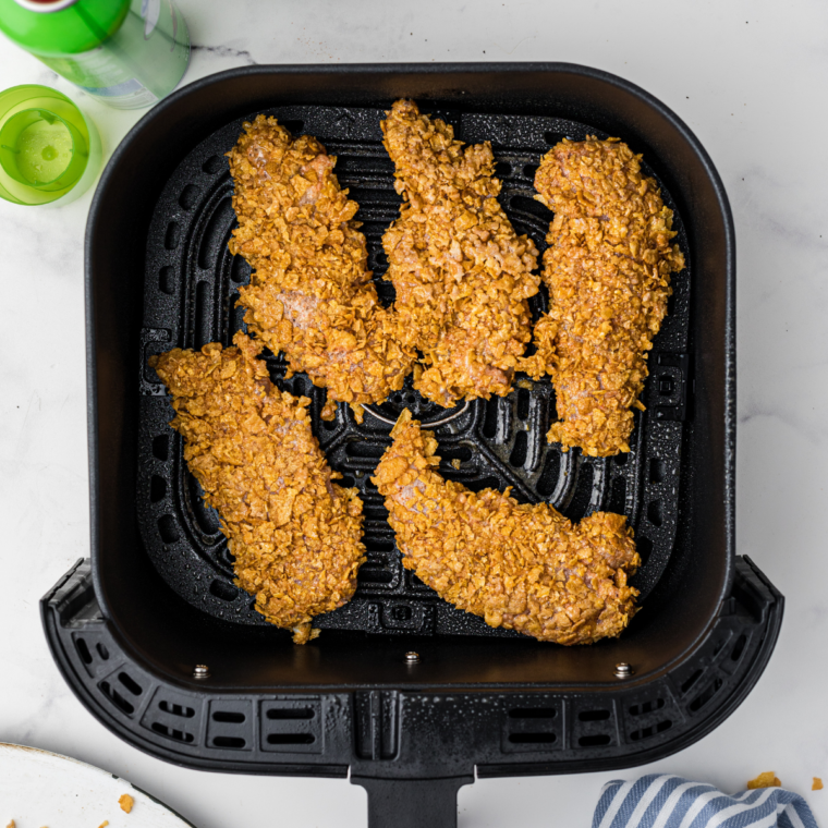 Golden-brown chicken tenders being removed from the air fryer basket with tongs.