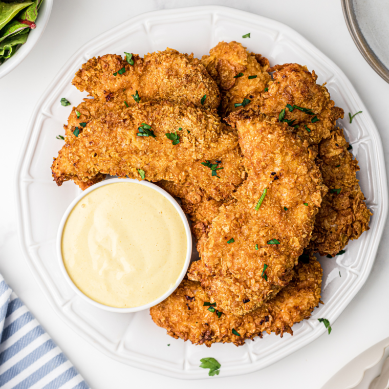  Crispy Air Fryer Chicken Tenders served on a plate with a small bowl of honey mustard sauce for dipping, garnished with fresh herbs.