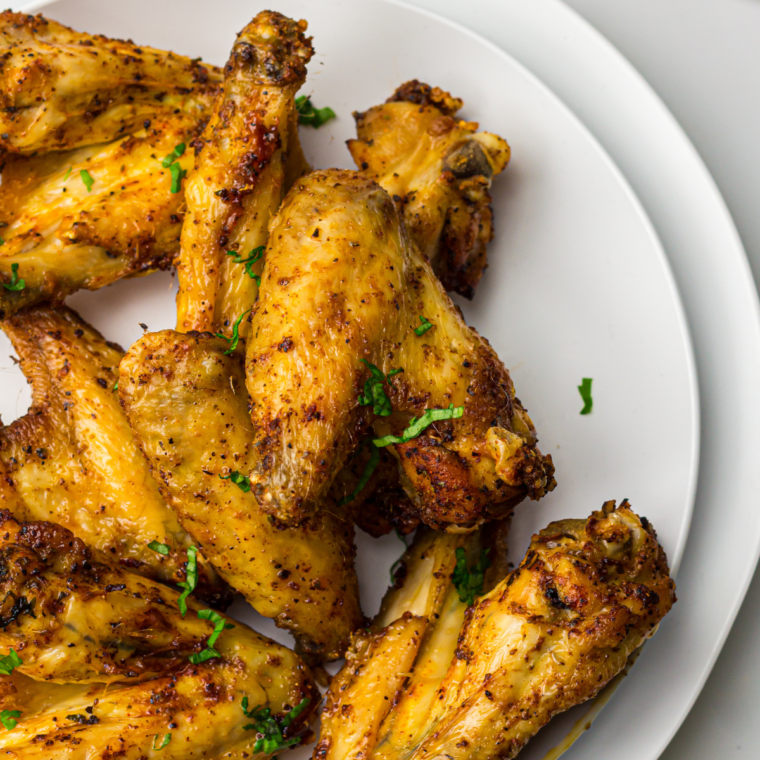 Cooked Chicken Wings on a plate with steakhouse seasoning and fresh herbs on top