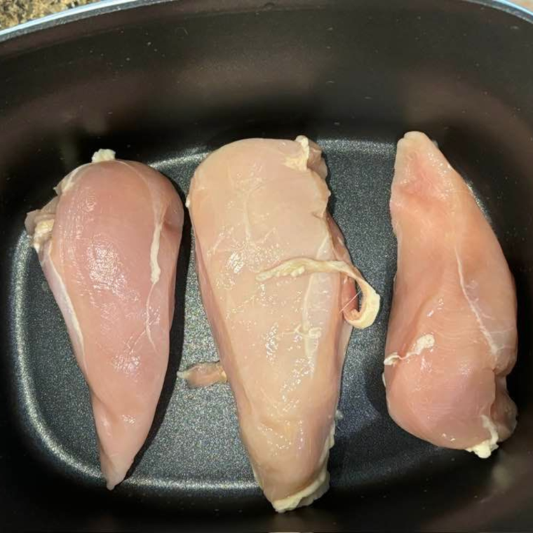 Boneless, skinless chicken breasts seasoned with kosher salt and black pepper on a cutting board.