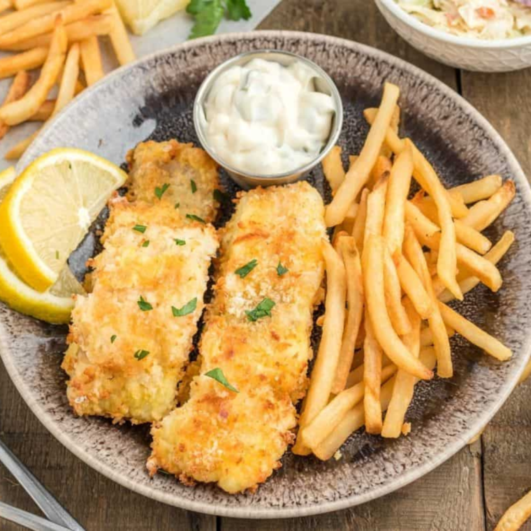 Plate of cooked cod on plate, with a side of tartar sauce, and French fries.
