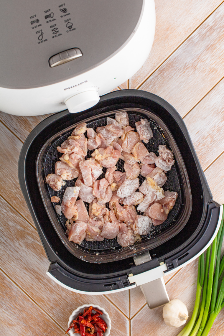 Placing seasoned chicken bites in a single layer in the air fryer basket.