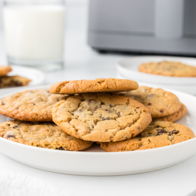 Close-up of warm, golden Air Fryer Toll House Cookies, featuring melted chocolate chips, placed on a white plate with a light background.