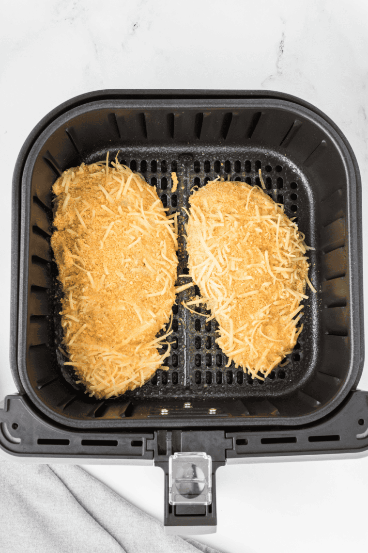 Two coated chicken breasts in the air fryer basket