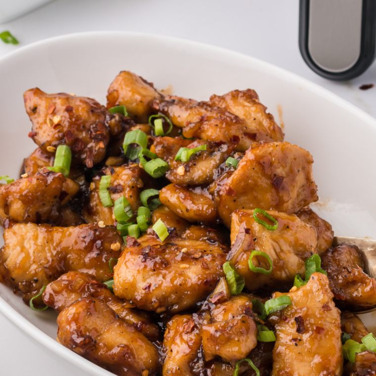 Crispy chicken nuggets coated in tangy sauce on white plate.