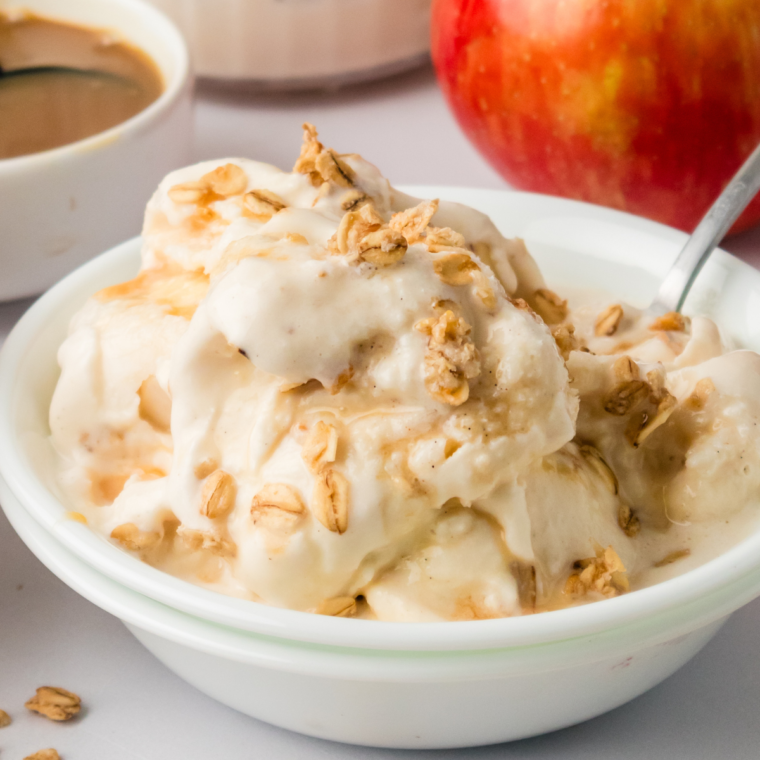 A bowl of freshly made Ninja Creami Apple Cobbler Ice Cream topped with crumbled cobbler and a scoop spoon beside it.