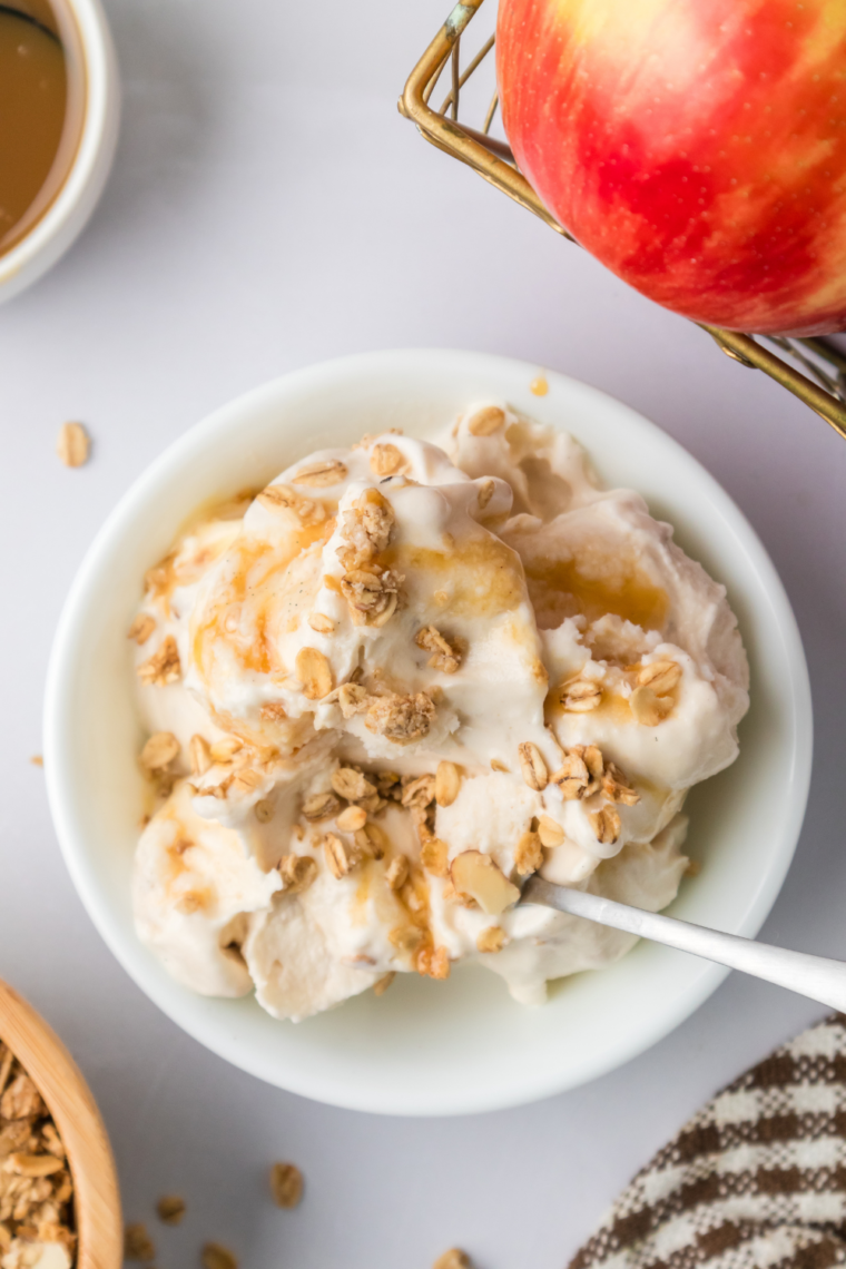 A bowl of creamy Ninja Creami Apple Cobbler Ice Cream topped with crumbled pie crust and cinnamon, garnished with a slice of apple.