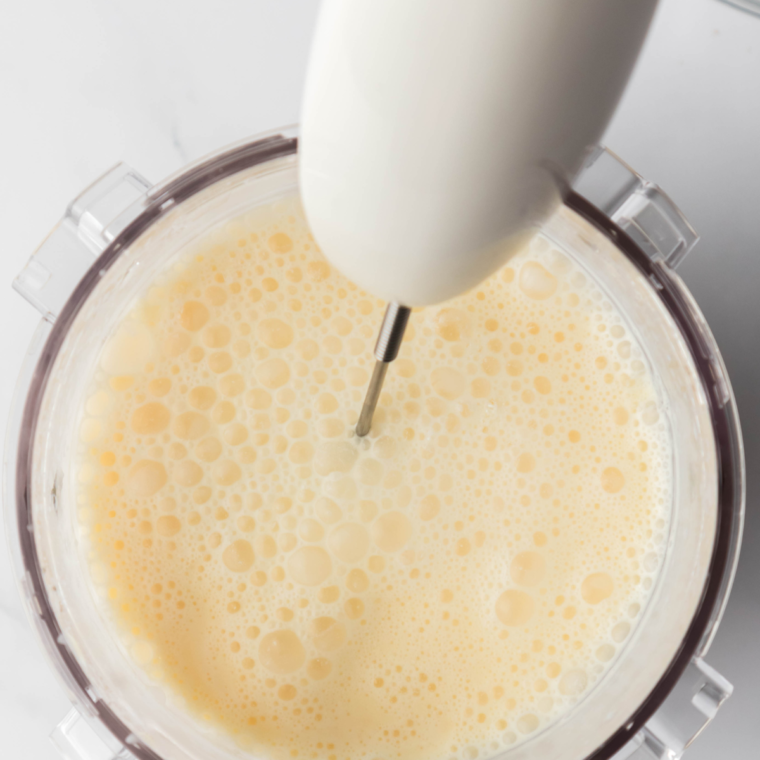 Adding heavy cream to the mixture for a creamy texture in the Ninja Creami Orange Julius.