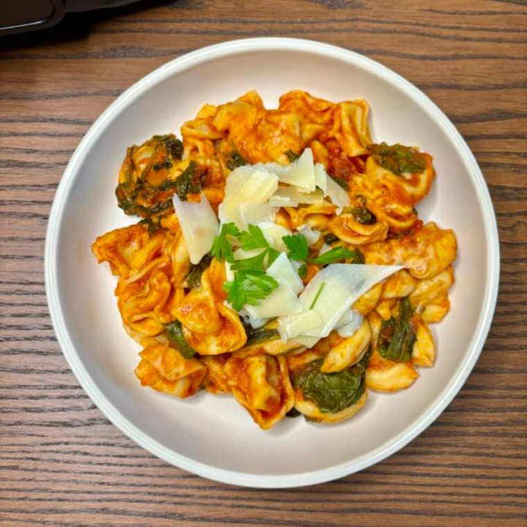 Plate of creamy tortellini made in the Ninja Foodi Possible Cooker Pro, garnished with fresh herbs.