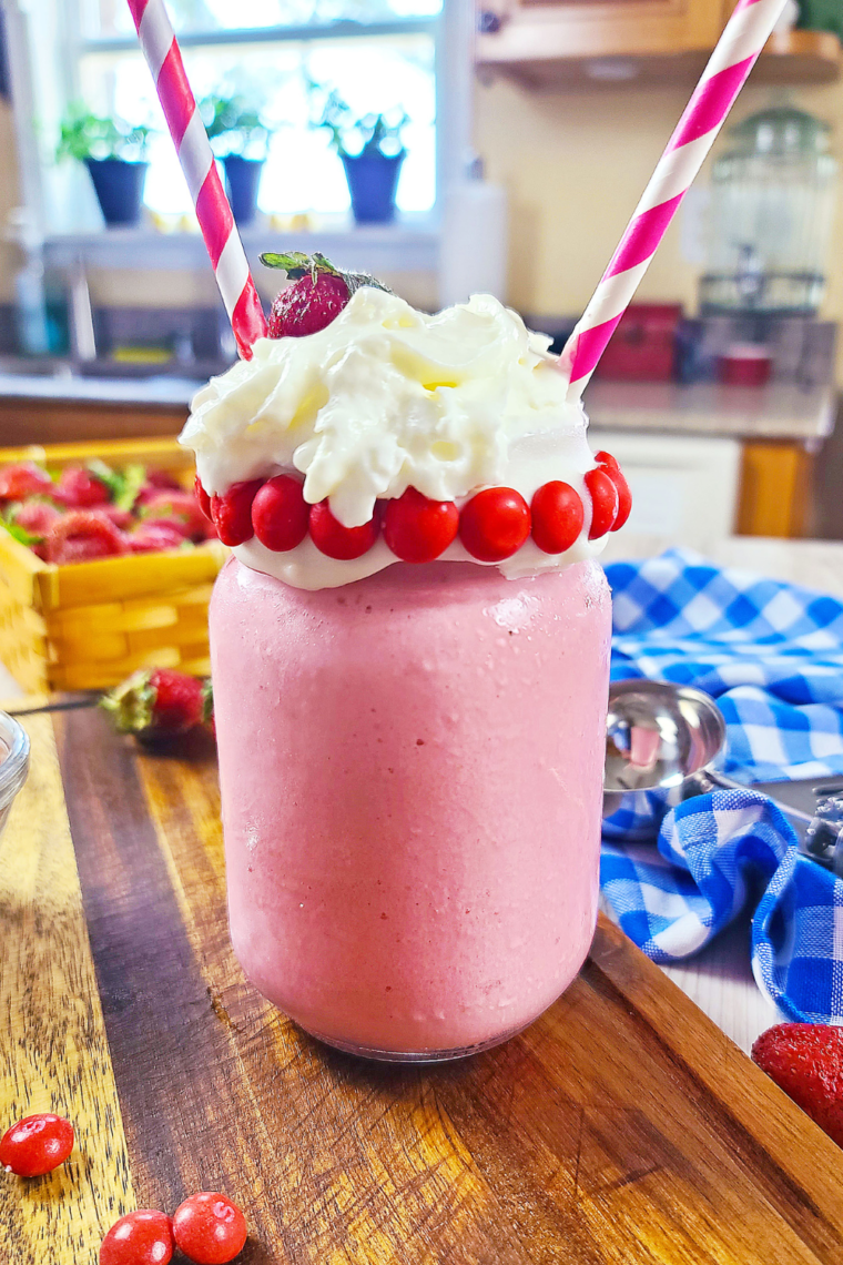 Strawberry frosty in a tall glass topped with whipped cream and a strawberry