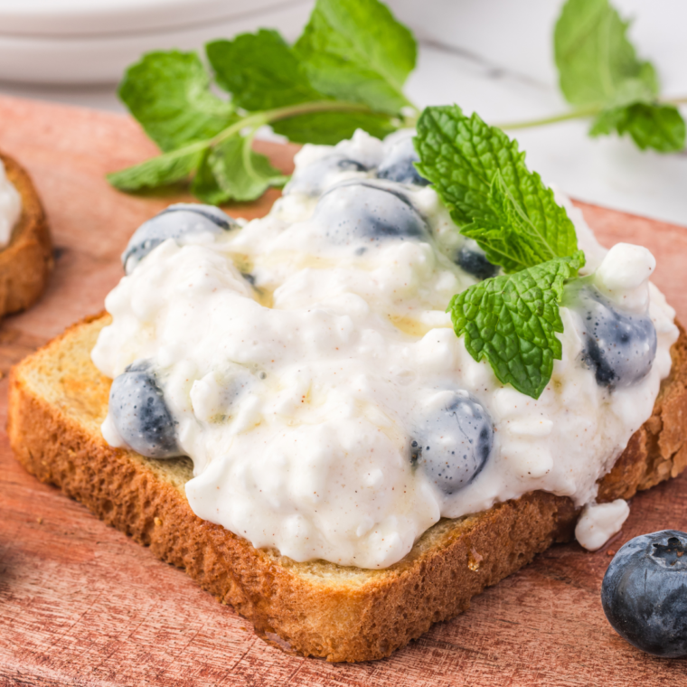 Close-up of crispy toast with creamy cottage cheese and vibrant blueberries, garnished with mint leaves.