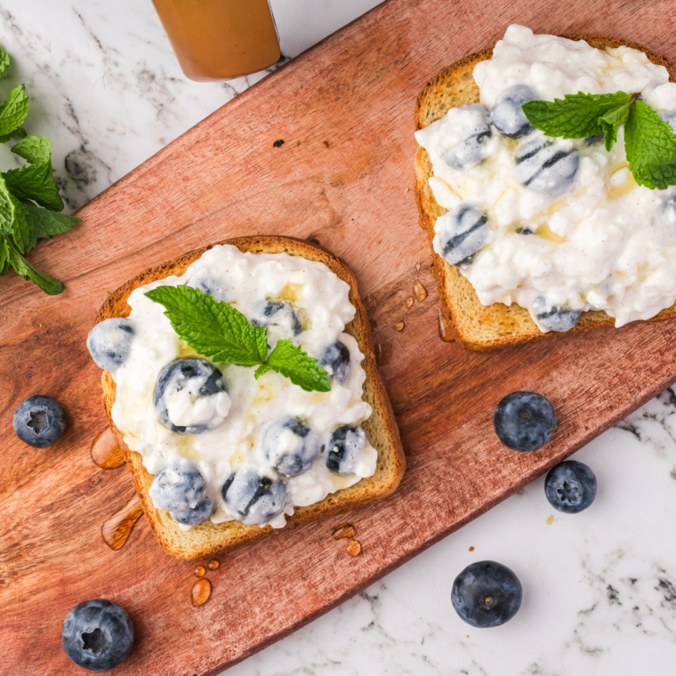 Air-fried blueberry cottage cheese toast served on a wooden cutting board, showcasing its delicious toppings.