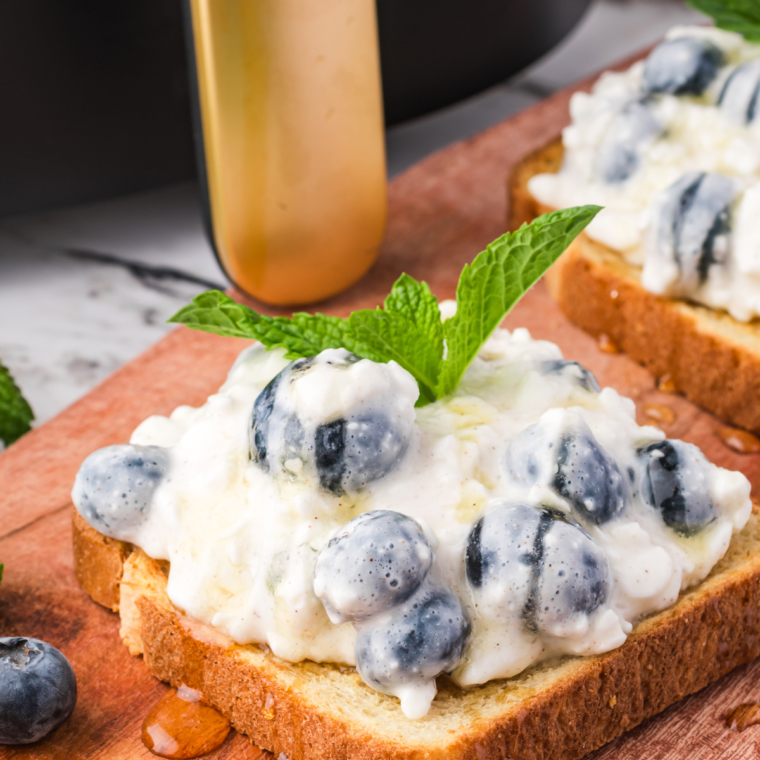 Delicious Air Fryer Blueberry Cottage Cheese Toast served on a white plate, featuring crispy golden bread topped with creamy cottage cheese and fresh blueberries, garnished with a sprinkle of cinnamon.