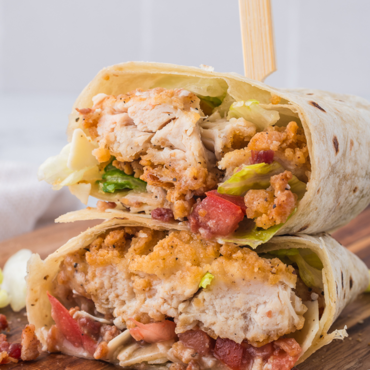 Air Fryer Caesar Wraps filled with crispy chicken, romaine lettuce, Caesar dressing, Parmesan cheese, and bacon bits served on a wooden board.