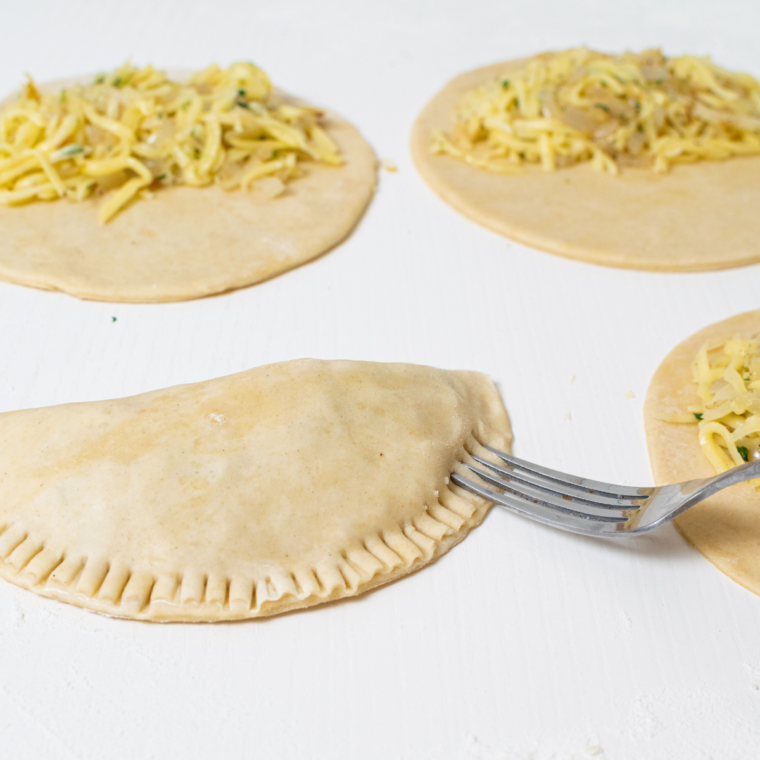 Folding pastry over cheese and onion filling to form a pasty.