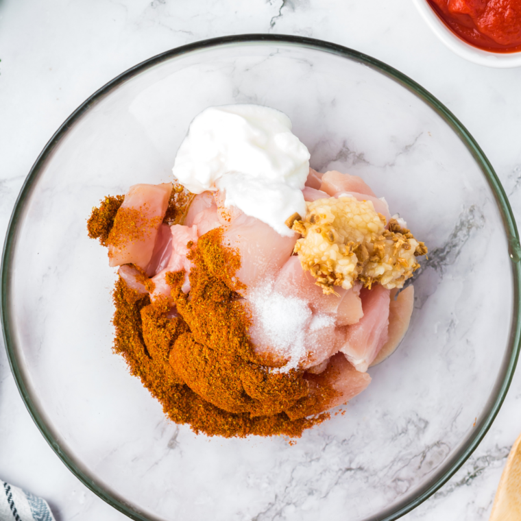 Close-up of a bowl with vindaloo spice mix, garlic paste, ginger paste, tomato paste, yogurt, and vinegar being whisked into a smooth marinade.