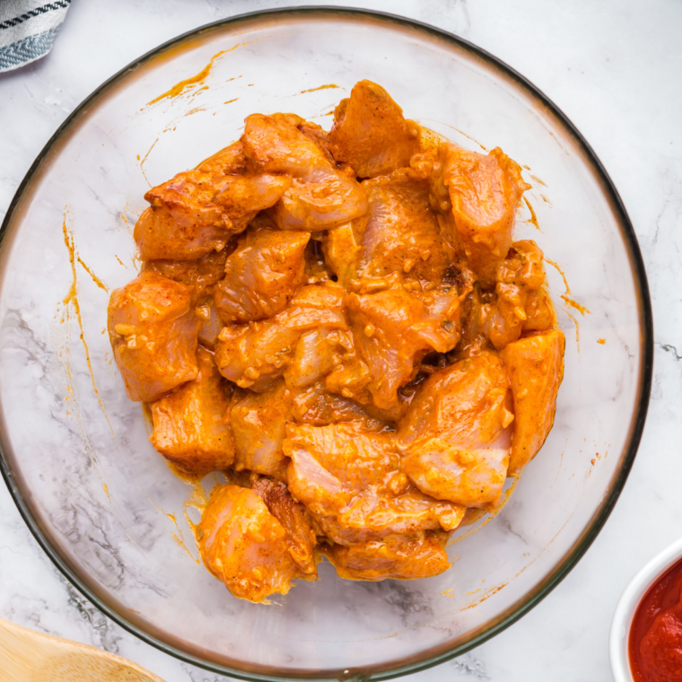 Chicken thighs being coated thoroughly with the prepared marinade in a bowl, showcasing the vibrant spice mix.