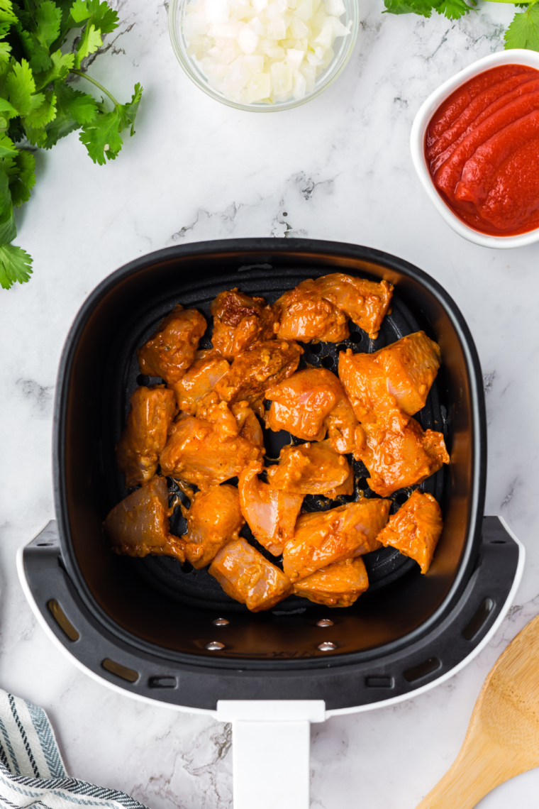 Marinated chicken arranged in a single layer in the air fryer basket, brushed lightly with oil, ready to cook.