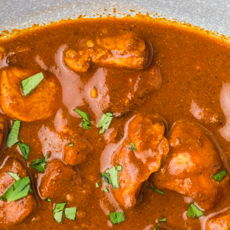 Plated chicken vindaloo garnished with fresh cilantro, served with rice and naan, presented as a complete and inviting meal.