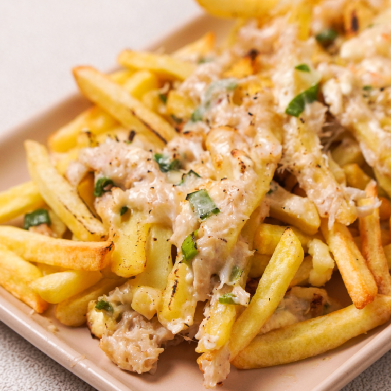 Golden fries topped with melted cheese and seasoned crab meat, garnished with fresh herbs, served on a plate