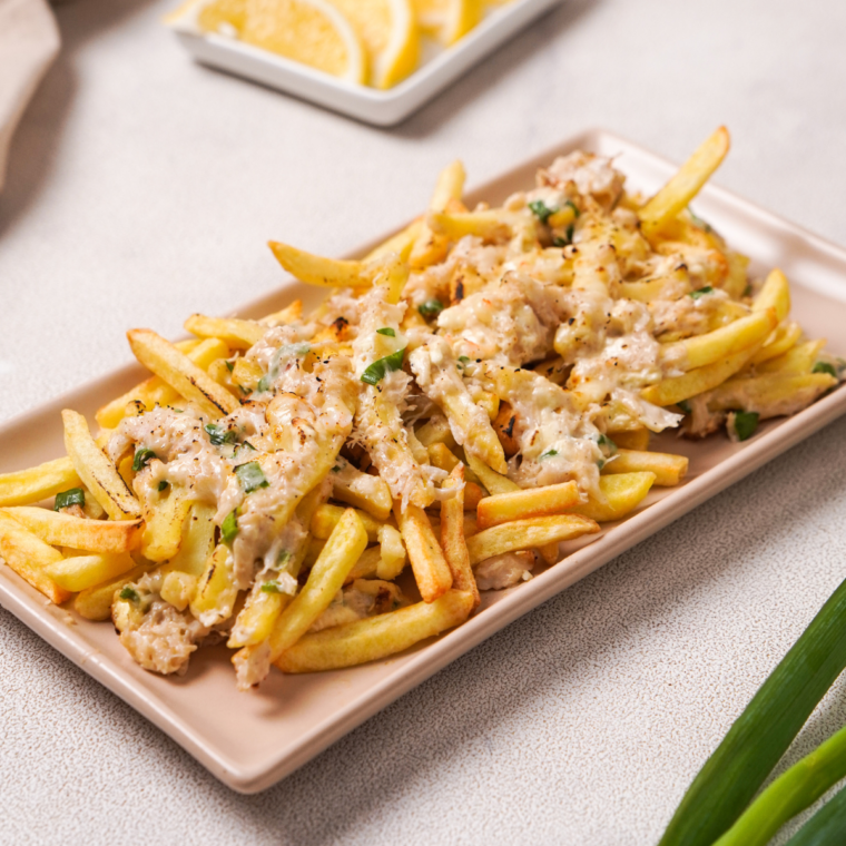 Golden-brown air fryer fries topped with melted cheese, seasoned crab meat, and fresh herbs, served on a plate for a delicious and easy appetizer.