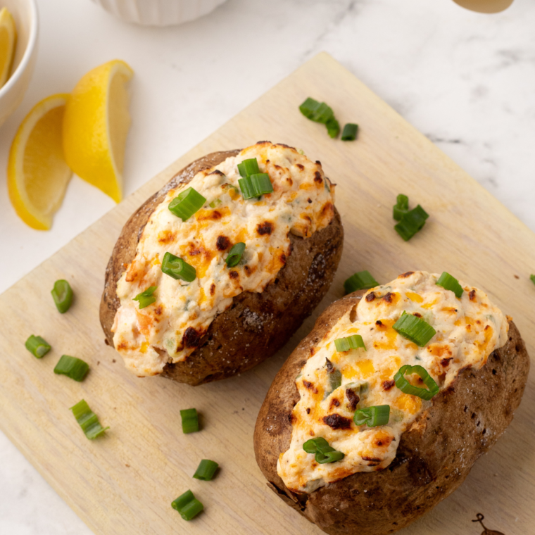 A baked potato topped with a creamy seafood mixture, including shrimp and crab, garnished with fresh herbs, served in a plate ready to enjoy.