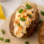 A loaded Air Fryer Seafood Baked Potato topped with creamy seafood filling, garnished with fresh herbs, served on a white plate.