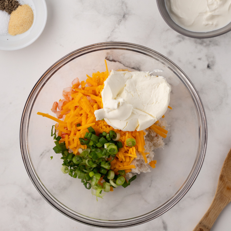 "Mixing bowl with cooked shrimp, crab meat, sour cream, cream cheese, green onions, cheddar cheese, garlic powder, and lemon juice ready for the seafood topping."