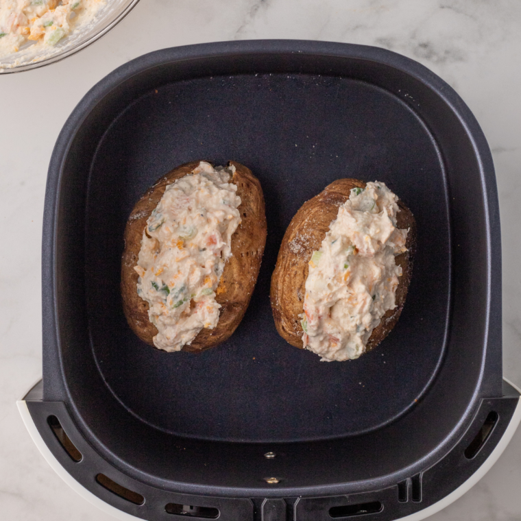 "Air fryer seafood baked potato with shrimp, crab, and creamy cheese topping, garnished with green onions and lemon wedges."