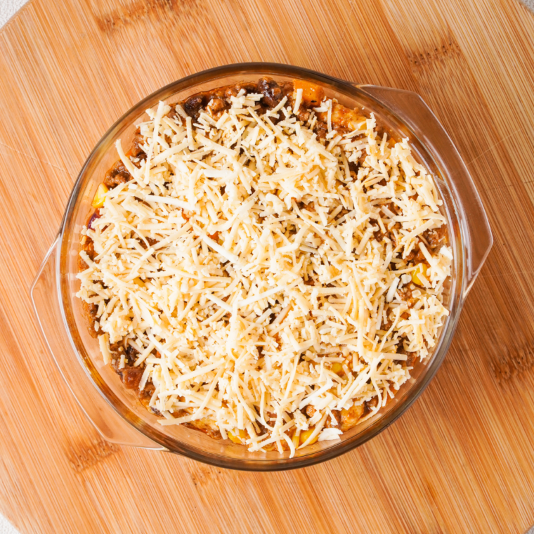 "Sprinkling shredded cheese over the layered ingredients for the bubble-up casserole."