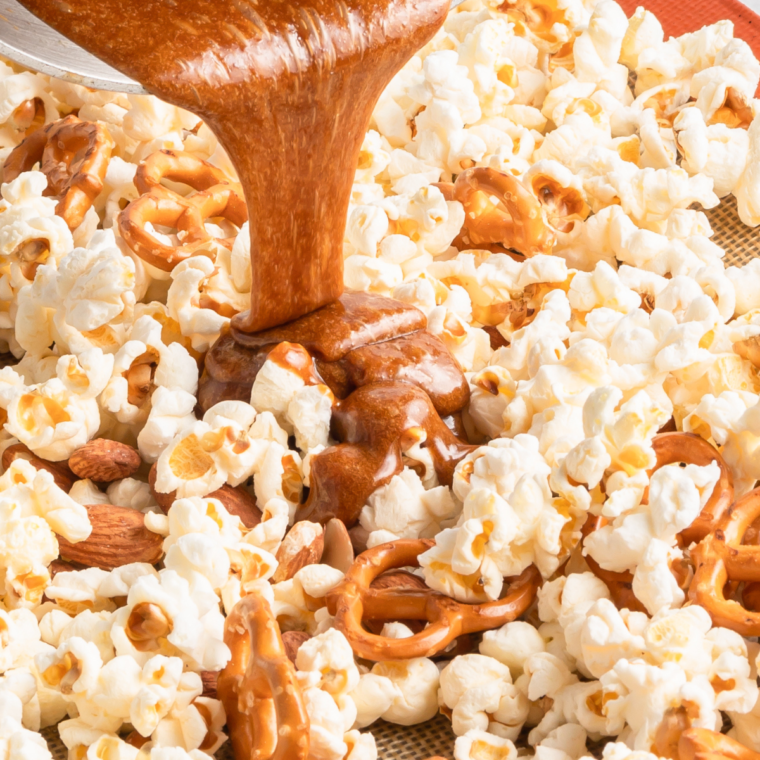 "Pouring rich caramel sauce over popcorn, almonds, and pretzels, stirring to coat evenly."