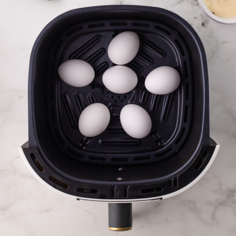 Air frying hard-boiled eggs in an air fryer basket at 270°F for 17-18 minutes before cooling them in ice water."