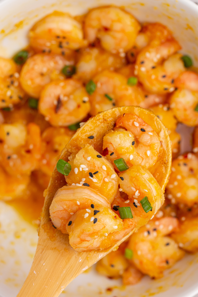 Close-up of crispy dynamite shrimp drizzled with spicy sauce, garnished with green onions and sesame seeds, served on a white plate."