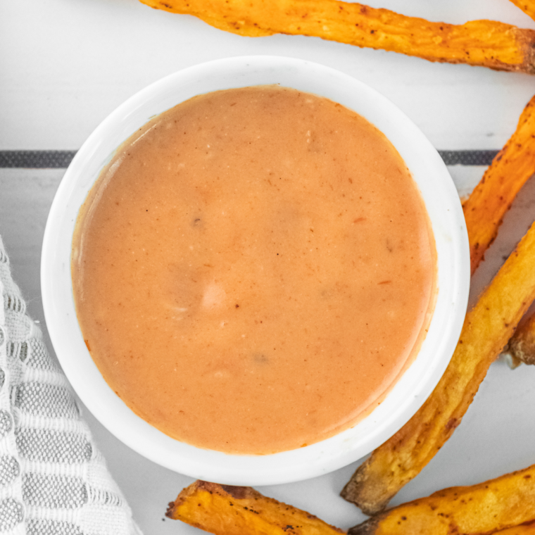 "A bowl of homemade Flamethrower Sauce with a creamy texture and vibrant orange color, surrounded by crispy fries ready for dipping."