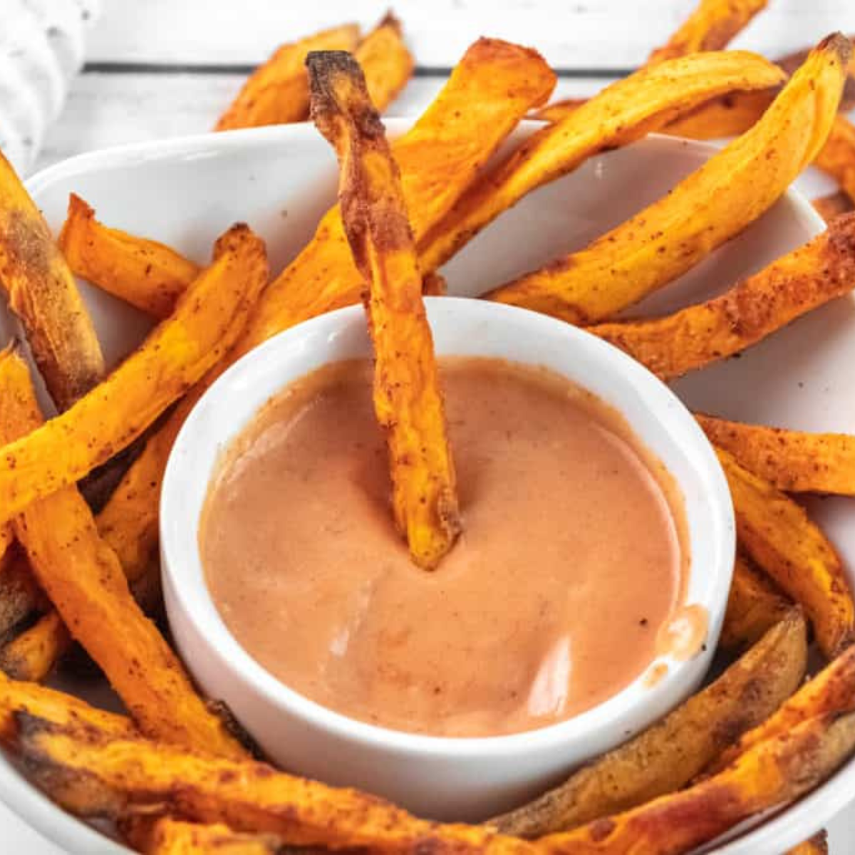 "A small bowl of spicy Flamethrower Sauce surrounded by dipping fries, showcasing its creamy and bold texture."