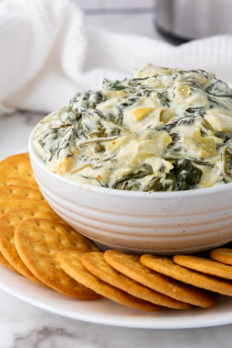 "Creamy spinach artichoke dip made in Ninja Foodi Possible Cooker Pro, with melted mozzarella and cream cheese, garnished with spinach."