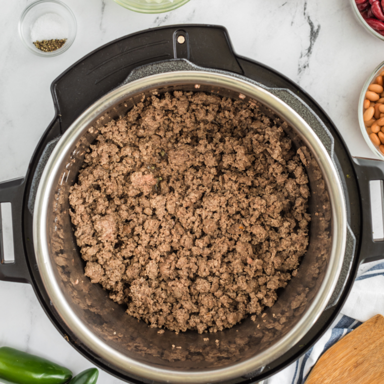 Ground turkey browning in the Instant Pot with a spatula, seasoned with salt and pepper.