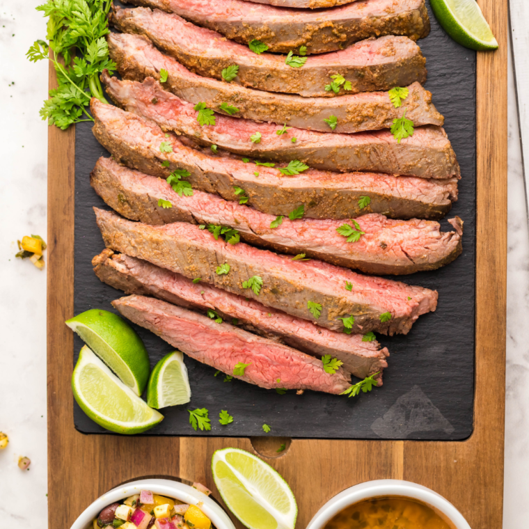 Steak sliced on a cutting board with lime wedges