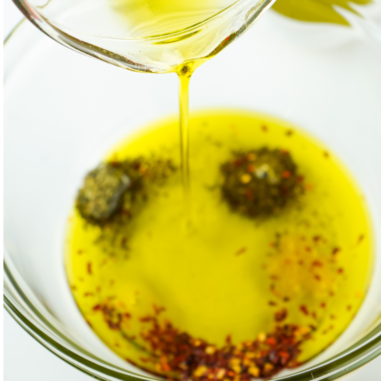 Pouring olive oil into a small bowl, adding balsamic vinegar, minced garlic, oregano, basil, and crushed red pepper flakes for Mediterranean bread dipping oil.